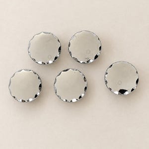 May include: Five circular buttons with a polished silver-tone finish and a scalloped edge design. Each button features a smooth, reflective surface and a consistent round shape, arranged in a group of five individual pieces for garment use.
