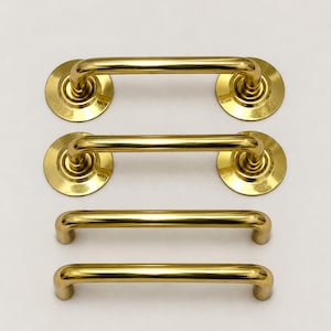 May include: Four polished brass cabinet pulls arranged in two rows. The top two pulls feature circular mounting plates at each end, while the bottom two pulls have simple cylindrical post mounts. All hardware has a smooth, reflective gold finish.
