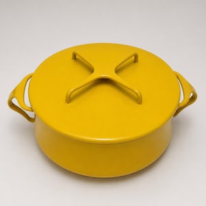 May include: A round, mustard yellow enameled cast iron Dutch oven with a matching lid. The lid features a distinctive X-shaped handle, and the pot includes two curved side handles for lifting. The entire exterior has a smooth, glossy finish.