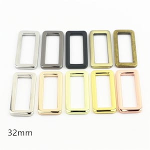 Puede incluir: Un conjunto de diez hebillas rectangulares de metal dispuestas en dos filas, con varios acabados que incluyen plata, bronce, negro mate, latón antiguo, oro pulido y oro rosa. Cada hebilla de metal mide 32mm de ancho.