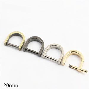 Puede incluir: Cuatro anillas en D de 20 mm con barra de tornillo extraíble. El conjunto incluye una anilla de latón, una de color bronce, una plateada y una dorada. Cada pieza tiene una parte superior curva y una barra base recta para su fijación.