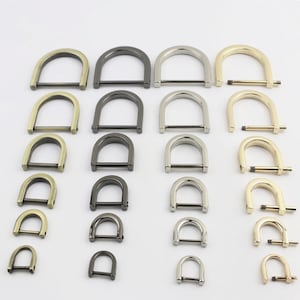 May include: A collection of metal D-rings arranged in four vertical columns and seven horizontal rows. The hardware pieces vary in size from large to small and feature four distinct metallic finishes: antique brass, gunmetal, silver, and gold.