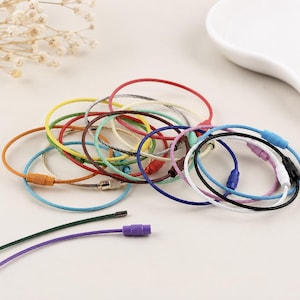 May include: A collection of circular wire keyrings in various colours including red, yellow, green, blue, orange, purple, black, and white. Each flexible metal cable features a threaded screw-type barrel connector for secure closure and attachment.