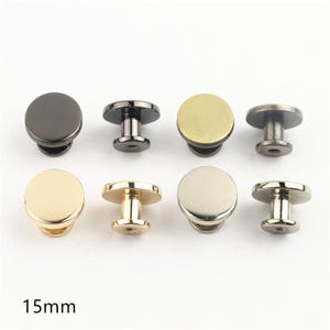 Può includere: Un set di otto bottoni a vite in metallo da 15 mm disposti su due file. I bottoni presentano una parte superiore circolare piatta e liscia e una base con perno filettato. Le finiture includono nero opaco, ottone anticato, oro e argento.