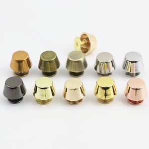 Può includere: Una collezione di dieci borchie metalliche a vite in varie finiture metalliche, tra cui oro, argento, rame, bronzo e canna di fucile. Ogni borchia presenta una forma conica con una parte superiore piatta e un meccanismo a vite visibile.