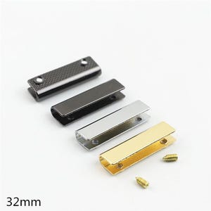 Könnte beinhalten: Vier rechteckige Kordelendkappen aus Metall mit einer Länge von 32mm, diagonal angeordnet. Das Set enthält eine texturierte schwarze, eine glatte schwarze, eine silberne und eine goldene Ausführung, jeweils mit zwei kleinen Schraublöchern und zwei passenden Schrauben.