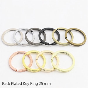 Puede incluir: Una colección de diez llaveros metálicos circulares dispuestos en dos filas. Los anillos presentan varios acabados metálicos, incluyendo plata, bronce, negro, bronce, oro rosa y oro. Cada anillo tiene un diámetro de 25 mm.