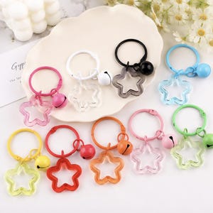 May include: A collection of ten circular keychains, each featuring a translucent star-shaped charm and a matching small jingle bell. The keychains come in various colors including pink, white, black, blue, yellow, red, orange, light pink, and green.