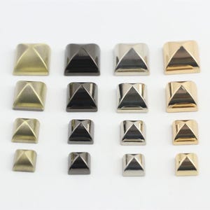Può includere: Una collezione di sedici borchie metalliche a forma di piramide quadrata disposte in una griglia quattro per quattro. Le borchie presentano quattro diverse finiture metalliche, tra cui ottone opaco, canna di fucile scuro, argento lucido e oro brillante.