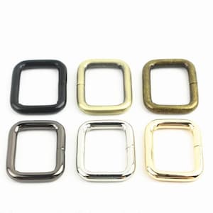 May include: Six rectangular metal loops arranged in two rows of three. The top row features a matte black loop, a brushed brass loop, and an antique bronze loop. The bottom row includes a gunmetal loop, a polished silver loop, and a gold loop.