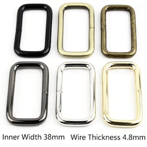 Puede incluir: Seis hebillas rectangulares de metal dispuestas en dos filas, con acabados en negro, oro mate, bronce antiguo, gris plomo, plata y oro brillante. Cada hebilla tiene un ancho interior de 38mm y un grosor de alambre de 4,8mm según el texto.