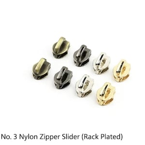 May include: A collection of seven No. 3 nylon zipper sliders in various metallic finishes, including antique brass, gunmetal, silver, and gold tones. Each slider features a smooth, curved pull tab and a compact, functional design for zippers.