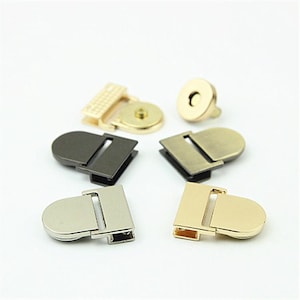 Puede incluir: Una colección de cierres metálicos para bolsos y broches magnéticos en varios acabados, incluyendo oro, plata, bronce y latón antiguo. Estos componentes de hardware presentan formas redondeadas y puntos de fijación rectangulares.