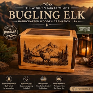 May include: A rectangular wooden cremation urn featuring a laser-engraved scene of an elk standing in a mountain landscape with pine trees. The box is constructed from light-colored wood with dark wood accents on the corners and top lid.