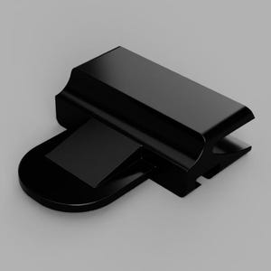 May include: A solid black plastic clip featuring a smooth, rectangular top section with a curved edge and a flat, rounded base extension. The component has a distinct geometric profile with a recessed channel along the side and a wedge-shaped protrusion.