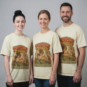 May include: A cream-colored short-sleeve t-shirt featuring a graphic print of a person with a camera and a child in a pumpkin patch. The text reads PUMPKIN PATCH and CREATIVE DIRECTOR, with a small sign saying ONE SMILE FOR MOM, ONE DONUT FOR YOU.