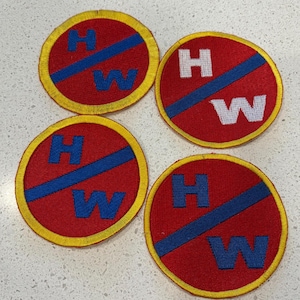 May include: Four circular patches with a red background, a blue diagonal stripe, and yellow trim. Each patch features the letters "H" and "W" in white or blue. The patches are arranged on a light-colored surface.