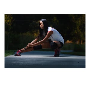 May include: A white athletic jersey with red trim, black shorts, black knee pads, and red and black trainers. The jersey features the number 21 on the back. The attire is designed for sports activities, providing a functional look for movement.