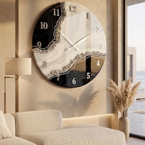 May include: A large circular wall clock featuring a split design of glossy black and white sections separated by a textured, silver-toned metallic vein. The clock face displays raised silver numerals from 1 to 12 and thin silver clock hands.