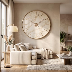 May include: A large circular wall clock featuring a beige and white marble-patterned face with a thin gold-toned metal frame. The clock has simple gold-toned hour markers and two slender gold-toned hands centred on the marble surface.