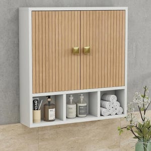May include: A wall-mounted white cabinet featuring two doors with vertical light wood slats and gold square knobs. Below the doors are three open storage compartments containing a toothbrush holder, two pump bottles, and stacked white towels.