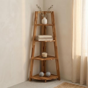 May include: A tall, light brown wooden corner shelf unit with four triangular tiers. The top shelf holds a white vase with dried greenery, the second holds two stacked books, the third holds a glass candle, and the bottom holds two grey spheres.