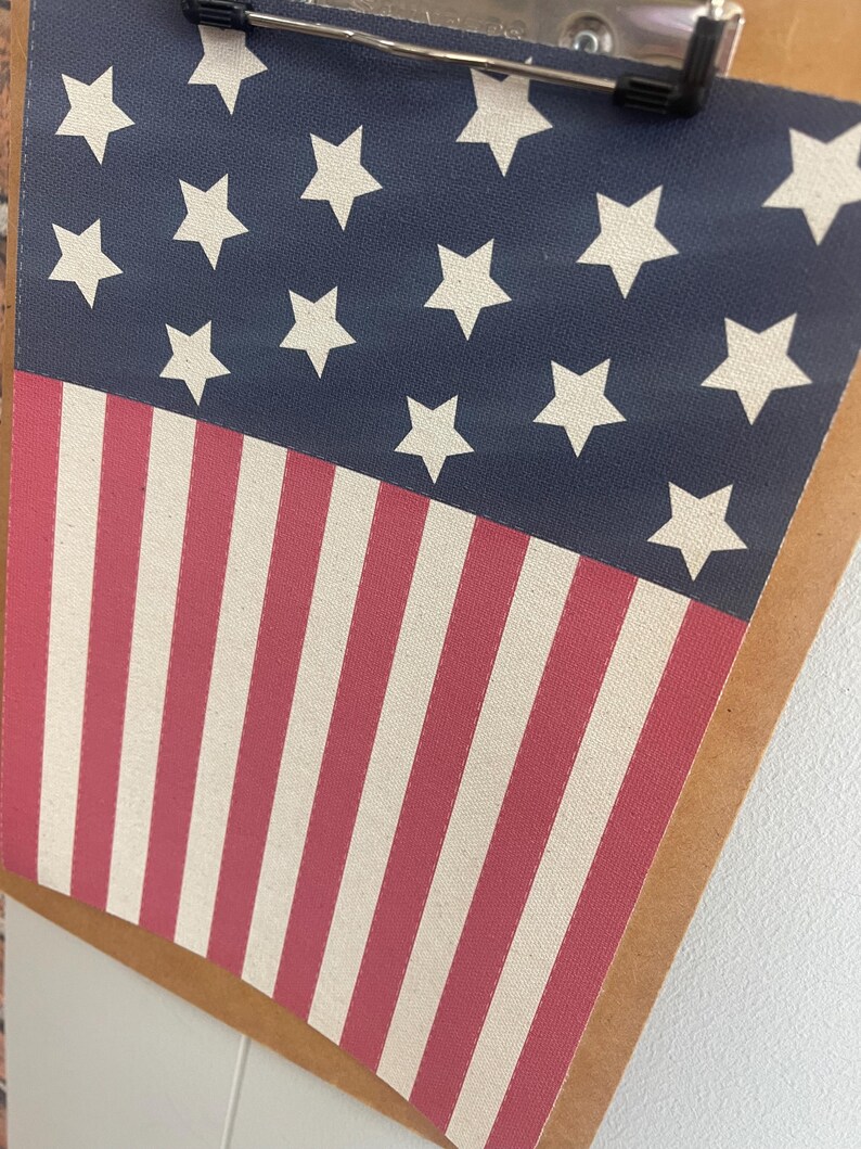 May include: A clipboard featuring a patriotic design. The top portion displays a navy blue background with white stars, while the bottom half showcases red and white stripes. The metal clip is visible at the top.