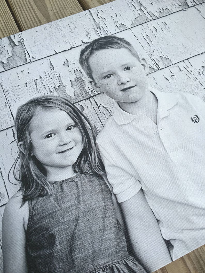 May include: A black and white photograph of a young girl and boy standing in front of a weathered wooden wall. The girl is wearing a sleeveless denim dress and the boy is wearing a white collared shirt with a logo on the pocket.