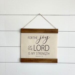 May include: A wooden framed canvas wall hanging with the text "For the joy of the Lord is my strength" and the scripture reference "Nehemiah 8:10".