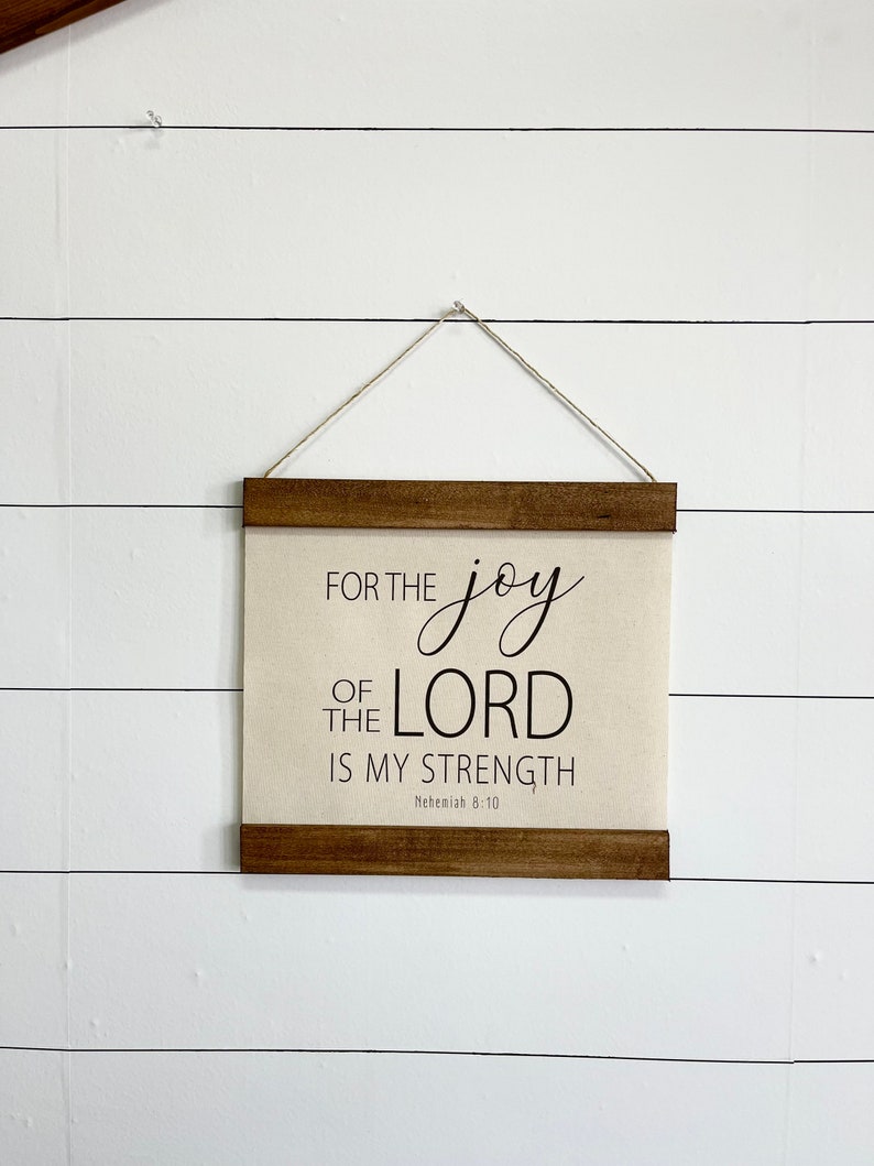 May include: A wooden framed canvas wall hanging with the text "For the joy of the Lord is my strength" and the scripture reference "Nehemiah 8:10".