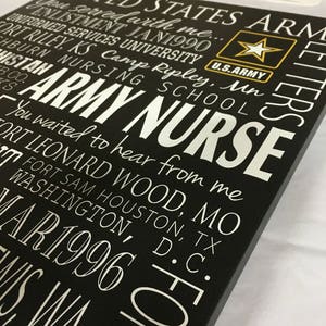 May include: Black wooden sign with white text that reads "UNITED STATES ARMY NURSE" and includes a list of military bases and dates. The sign also features a gold star with the words "U.S. ARMY" underneath.