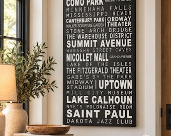 May include: A rectangular black canvas wall art piece featuring white text listing various Minneapolis and Saint Paul landmarks, including Como Park, Mississippi River, Summit Avenue, Nicollet Mall, Uptown, and Lake Calhoun in a bold font.