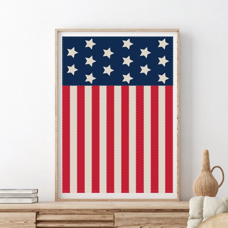 May include: Framed print featuring the American flag design. The top section has a navy blue background with white stars. The bottom section has red and cream-colored vertical stripes. The print is in a wooden frame.