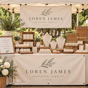 Puede incluir: Un puesto de joyería con una pancarta que muestra el texto LOREN JAMES HANDMADE JEWELRY y un gráfico de hojas. La exhibición incluye bustos para collares, soportes de madera para pendientes y un letrero TIMELESS PIECES FOR EVERYDAY BEAUTY.