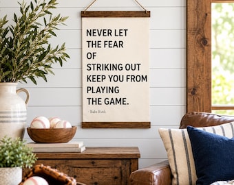 May include: A rectangular canvas wall hanging with dark wood trim at the top and bottom, suspended by a brown cord. The off-white fabric features black text reading: NEVER LET THE FEAR OF STRIKING OUT KEEP YOU FROM PLAYING THE GAME. - Babe Ruth