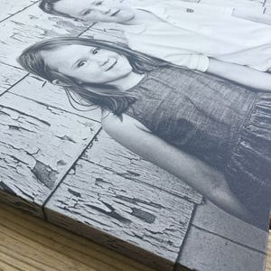 May include: Black and white photograph of two children, a girl and a boy, posing in front of a weathered wooden wall. The girl is wearing a dark dress and the boy is wearing a white shirt.