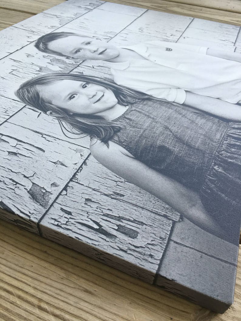 May include: Black and white photograph of two children, a girl and a boy, posing in front of a weathered wooden wall. The girl is wearing a dark dress and the boy is wearing a white shirt.