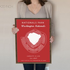 May include: A red and white print of Nationals Park, home of the Washington Nationals baseball team. The print includes the stadium's seating chart, the team's name, and the stadium's capacity and establishment date. The print is framed in a brown wood frame.