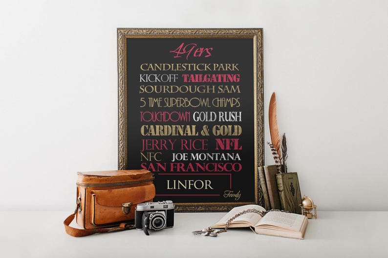 May include: A black framed chalkboard with gold lettering lists facts about the San Francisco 49ers football team. The text includes "Candlestick Park", "Tailgating", "Sourdough Sam", "5 Time Superbowl Champs", "Touchdown Gold Rush", "Cardinal & Gold", "Jerry Rice NFL", "NFC Joe Montana", "San Francisco", and "Linfor".