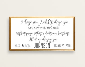 May include: A gold framed print with a white background and black calligraphy text. The text reads "I choose you. And I'll choose you over and over and over. Without pause, without a doubt, in a heartbeat. I'll keep choosing you." Below the text is "MILES & LAYLA JOHNSON EST MAY 26, 2018".