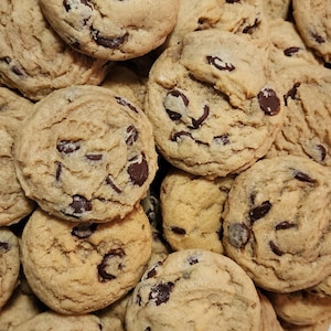 May include: A pile of freshly baked chocolate chip cookies. The cookies are golden brown with visible chocolate chips throughout. The image shows a close-up view of the cookies, highlighting their texture and appearance.
