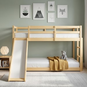 May include: A light-colored wooden bunk bed featuring a built-in slide on the left side, a ladder on the right, and safety rails on the top bunk. The bed is dressed with white mattresses and a mustard yellow throw blanket on the bottom bunk.