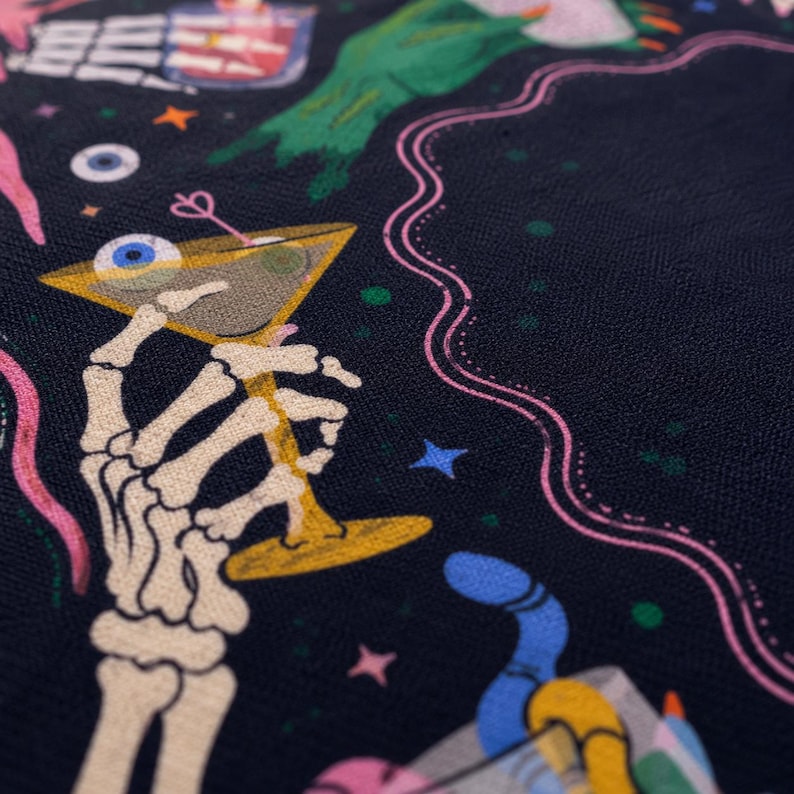 May include: A black fabric featuring a colorful graphic print of a skeleton hand holding a martini glass with an eyeball inside. The design includes additional elements like a green hand, pink wavy lines, blue stars, and small colorful dots.