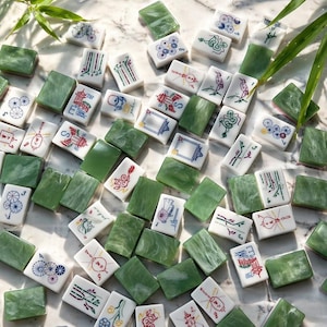 May include: A collection of rectangular Mahjong tiles featuring a mix of solid green marbled surfaces and white tiles with colorful illustrations of traditional motifs, including pagodas, bamboo, dragons, and floral patterns.