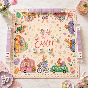 May include: A square game mat featuring a cream background with colorful illustrations of rabbits, Easter eggs, and flowers. The text Happy Easter is printed in the center. The mat includes three clear tile racks with purple tiles and several white mahjong tiles.