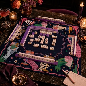 May include: A mahjong game set featuring a dark blue play mat with colorful illustrations of hands, brains, and eyes. The set includes white tiles with purple backs, purple tile racks, and a score pad. The tiles display various traditional symbols.