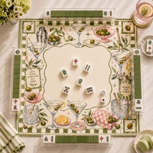 May include: A square mahjong mat featuring a martini-themed illustration with cocktail glasses, olives, and shakers. The mat includes four clear tile racks containing green and white mahjong tiles. Five loose tiles and two dice are placed in the center.