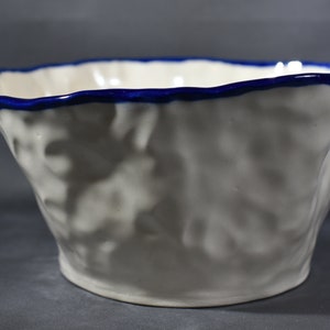 May include: White ceramic bowl with a blue rim. The bowl has a textured, organic shape.