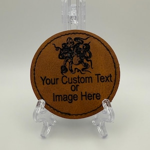 May include: A circular brown leather patch featuring a black laser-engraved octopus graphic and the text "Your Custom Text or Image Here" centred on the surface. The patch is displayed on a clear plastic stand with visible black stitching.