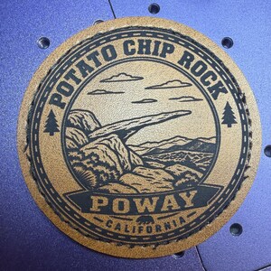 May include: A circular tan leather patch featuring a black engraved illustration of Potato Chip Rock in Poway, California. The design includes a thin rock formation, clouds, and pine trees, with the text POTATO CHIP ROCK and POWAY CALIFORNIA.